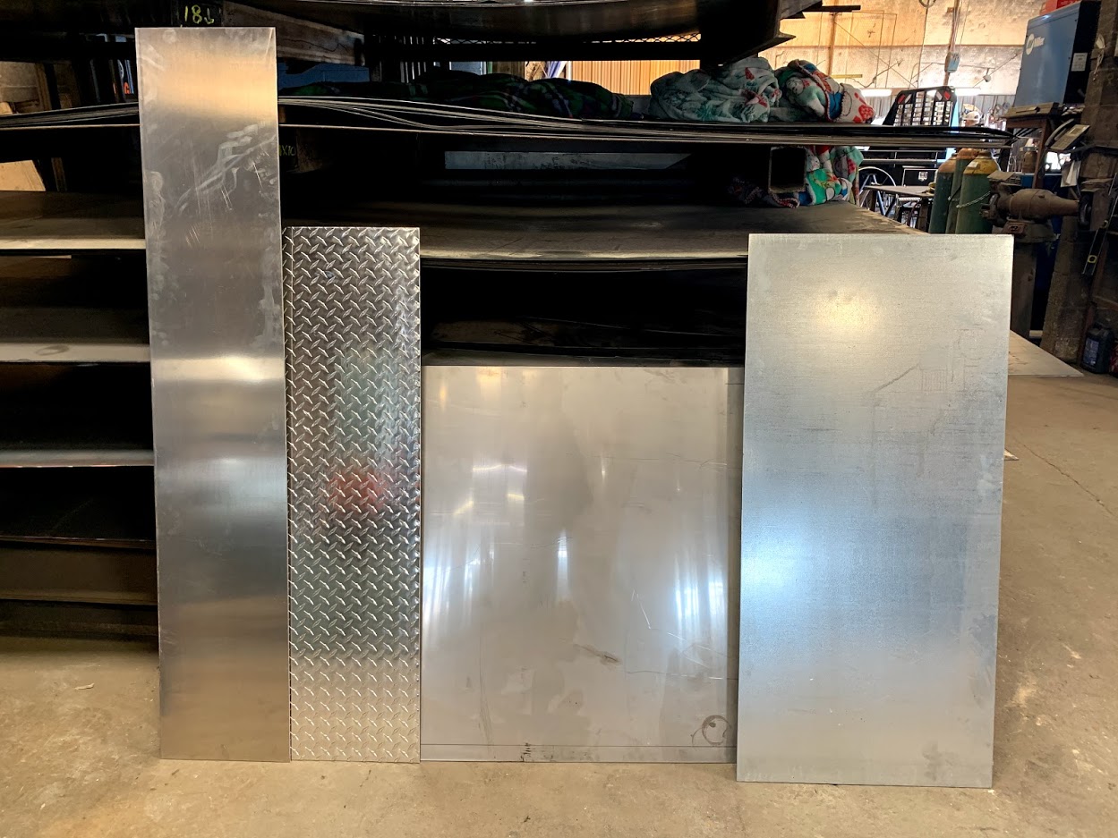 Plain aluminum, diamond-plate tread brite, and galvanized sheet metal samples on the shop floor at Riggs Machine & Welding, Stephenville, TX