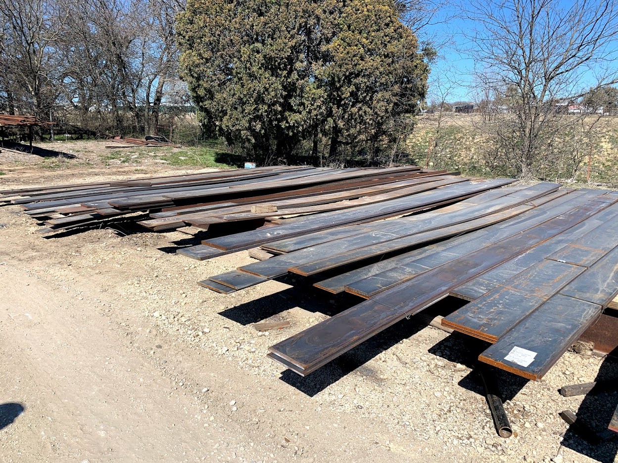 Hot roll and cold roll steel flat bar in long lengths stacked outdoors at Riggs Machine & Welding, Stephenville, TX