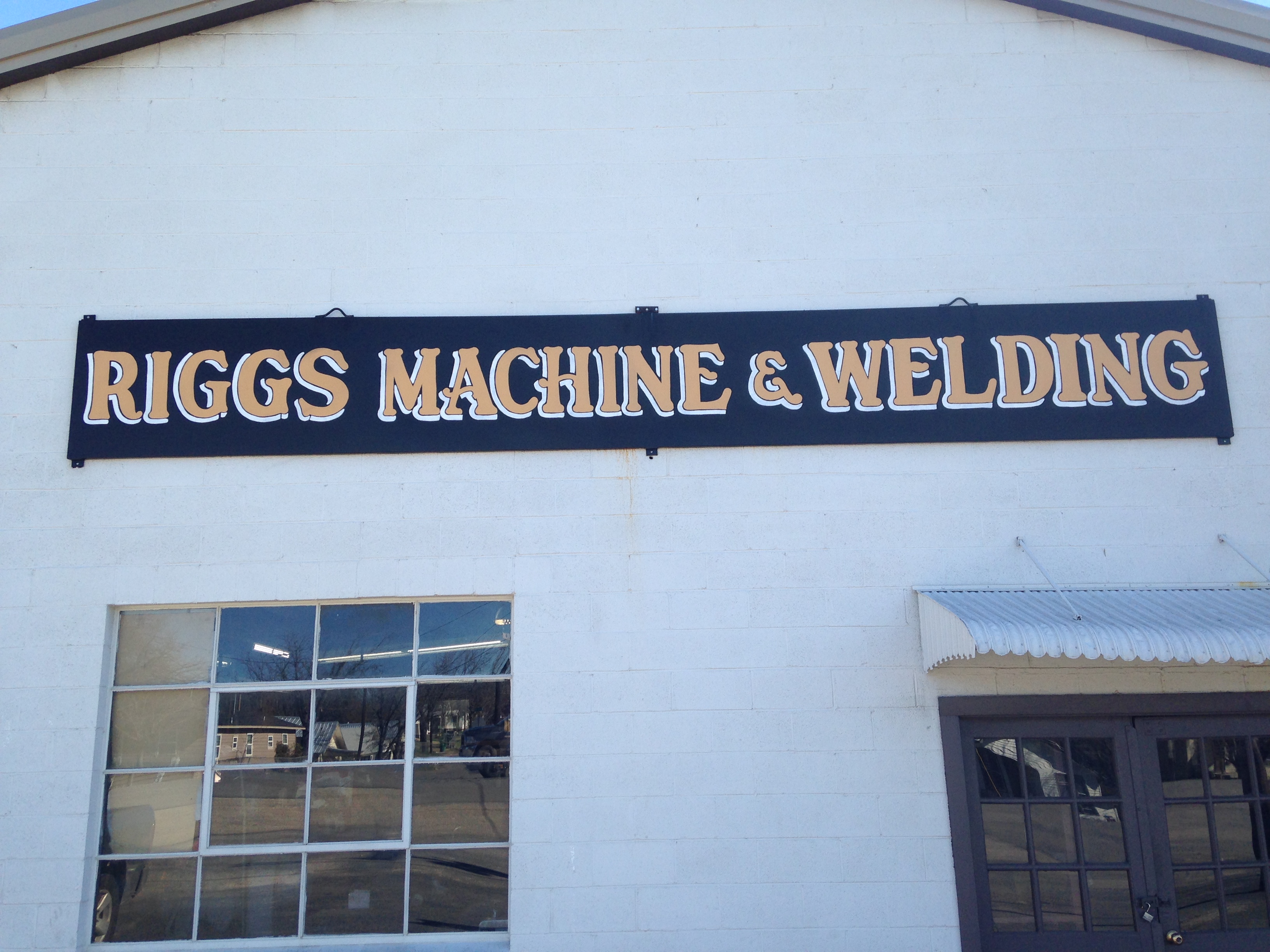 Exterior of the Riggs Machine & Welding building in Stephenville, TX, with the painted shop sign on white brick