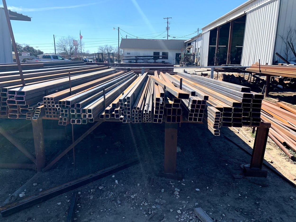 Square and rectangular tubing mixed with round tube on a rack outside Riggs Machine & Welding shop in Stephenville, TX