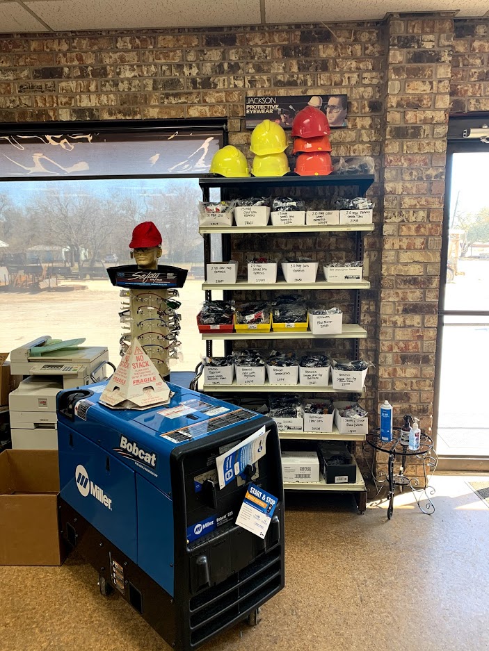 Interior of Riggs Machine & Welding supply floor in Stephenville, TX showing Miller Bobcat welder for sale, hard hats, and Jackson safety glasses display